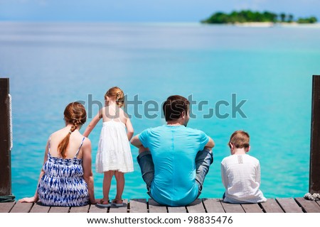 Family on wooden dock looking to ocean and tropical fishes