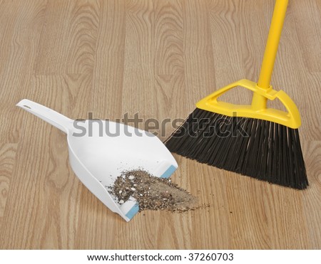 Broom sweeping up dirt into dust pan on hardwood floor