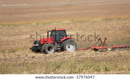 Red farm tractor discing a farm field after harvest