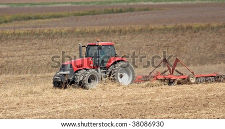 Red farm tractor discing a farm field