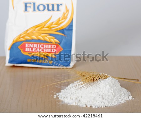 Pile of flour with two wheat stalks with a bag of flour in background