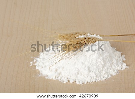 Pile of wheat flour with two wheat stalks on a wood table