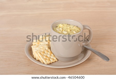 Cup of chicken noodle soup with crackers on a wood table