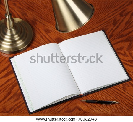 Opened notebook on a desk with lamp and pen