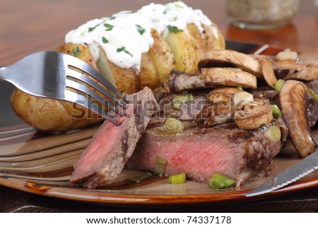 Steak covered with mushrooms and a baked potato with sour cream