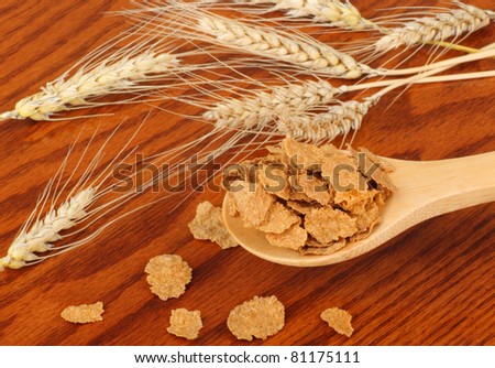 Wheat flakes on a spoon with wheat heads on a table