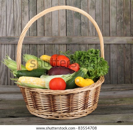 Harvested vegetables and fruits in a basket against a weathered fence