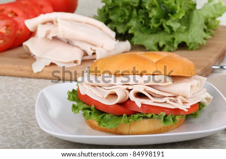 Turkey, lettuce and tomato sandwich on a plate with tomatoes, turkey and lettuce in background
