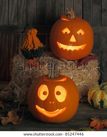 Two smiling jack-o-lanterns one on a wood floor and one on a straw bail
