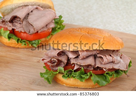 Two roast beef sandwiches with lettuce and tomato on a cutting board