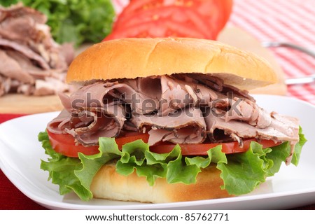 Closeup of a roast beef sandwich with lettuce and tomato on a white plate