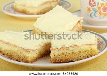 Three lemon squares on a plate with coffee cup in background