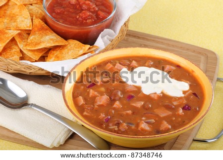Bowl of ham and bean soup with sour cream and tortilla chips and salsa in background