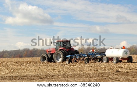 Red tractor pulling plow and anhydrous ammonia tank