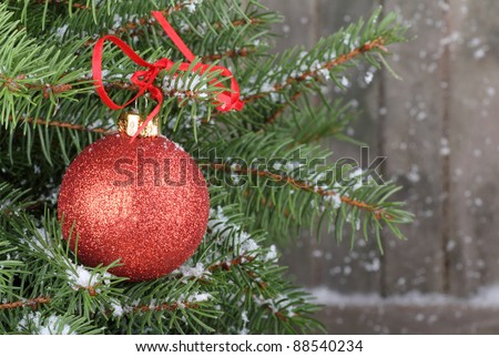 Red Christmas tree on snowy branches with snow falling in background