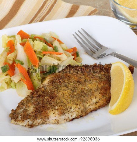 Breaded fish fillet with vegetables and lemon slice on a plate