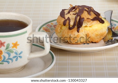 Cream puff on a plate with a cup of coffee