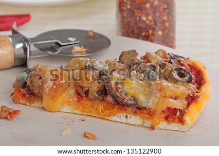 One pizza slice on a platter with a pizza cutter