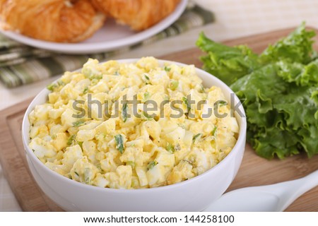 Egg salad in a bowl with lettuce on the side for making sandwiches
