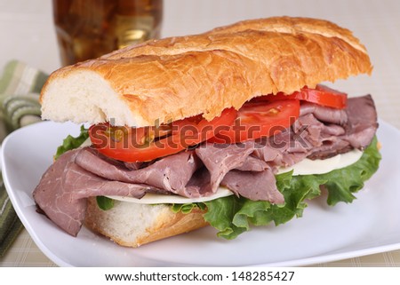 Sandwich with roast beef cheese lettuce and tomato on french bread on a plate