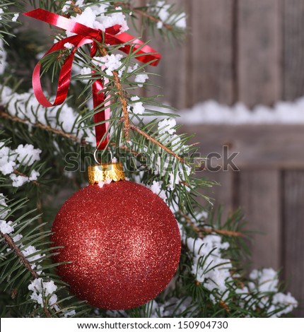 Red Christmas ball hanging from snowy evergreen branch with wood background