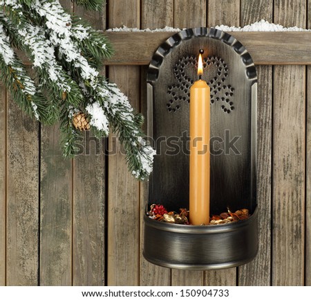 Burning gold candle hanging on a wood fence with snowy evergreen tree branch