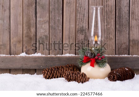 Burning christmas oil lamp in the snow with wood fence background