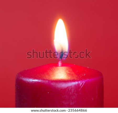 Closeup of a burning red candle on a red background