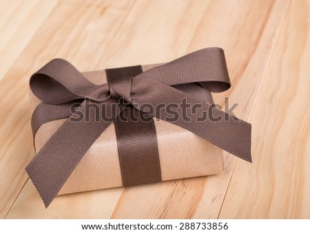 Gift package wrapped in ribbon and bow on wood surface