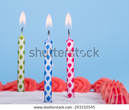 Three burning birthday candles on a cake with blue background