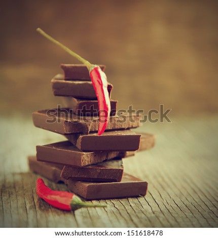 Red chili pepper on stack of dark chocolate pieces on wooden background