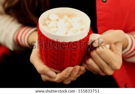 Hands holding mug of hot chocolate with marshmallows close-up
