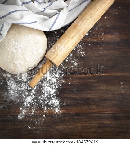 Classic wooden rolling pin with freshly prepared dough and dusting of flour on wooden background