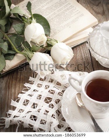 Cup of tea, books and roses on wooden table