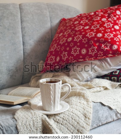 Still life interior details, cup of tea and book on the sofa with pillows