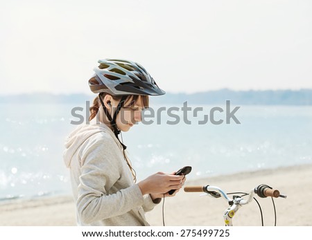 Teenage girl with bike listening to music on her phone at the beach. Toned image