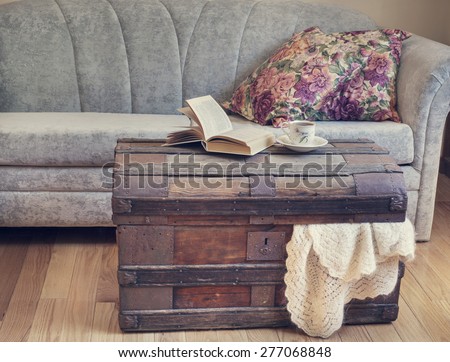 Still life interior details, book and cup of tea on old trunk near sofa