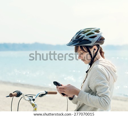 Teenage girl with bike listening to music on her phone at the be
