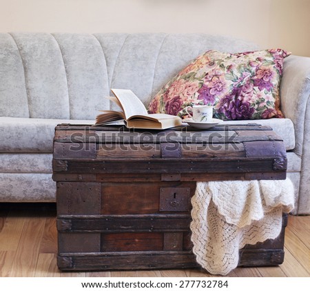 Still life interior details, book and cup of tea on old trunk near sofa