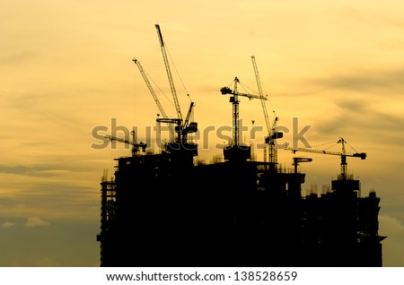 Silhouette Building crane and building under construction against evening cloudy sky