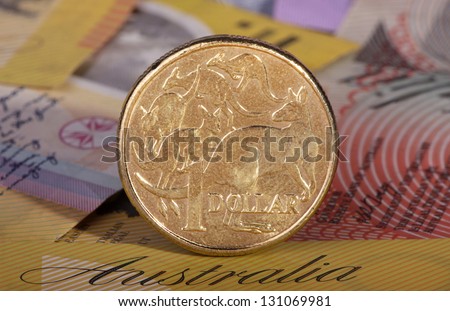 One Australian dollar coin with a background of Australian bank notes.