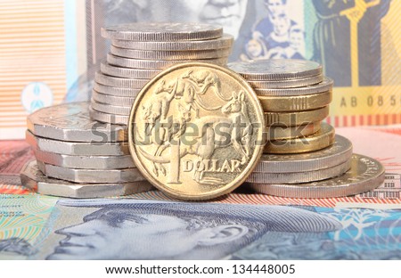 An Australian gold one dollar coin sits next to a stack of coins on top of Australian bank notes.