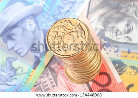 A tall stack of gold Australian one dollar coins sits on top of three Australian bank notes.