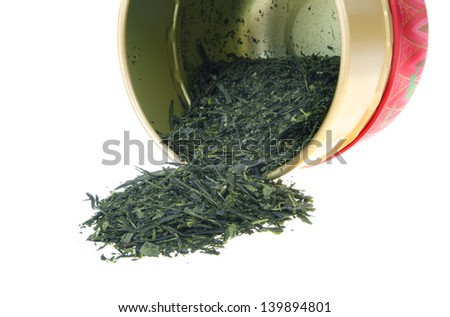 Japanese green tea leaf spilling from a red tea caddy isolated on white background.