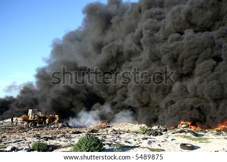 A bulldozer attempting to control a fire with lots of smoke at a refuse site