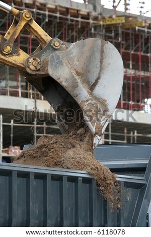 Back Actor filling a truck with earth at a building site with new building in background