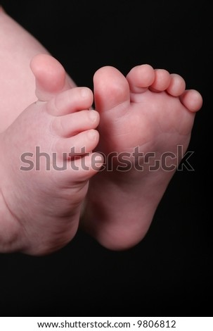 A tiny baby\'s feet and toes against a black background