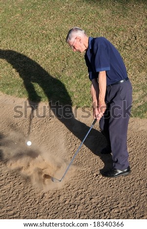 Senior golfer hitting ball out of golf sand trap
