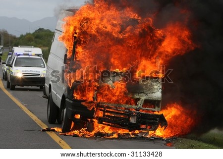 Panel van ablaze with huge flames and police car behind