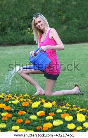 Pretty young lady with lovely smile watering flowers with a watering can